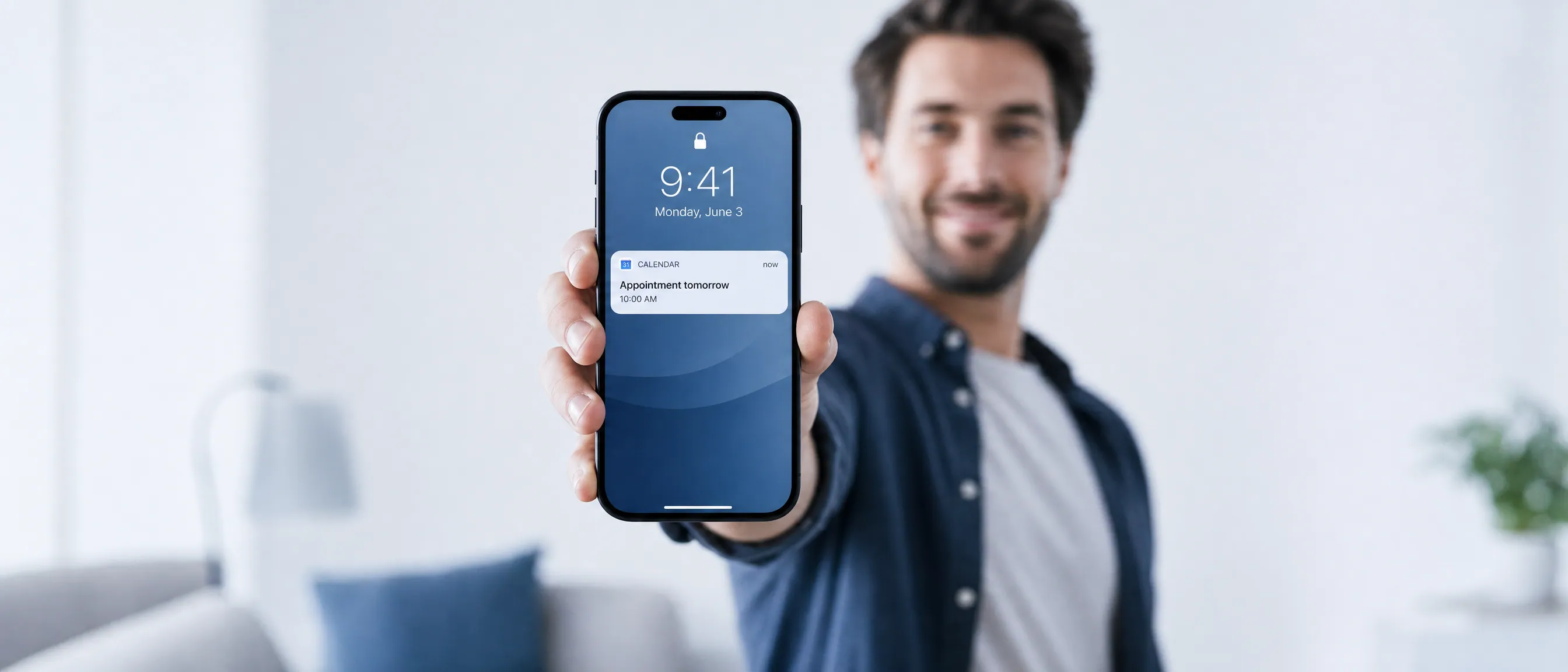A smiling person holding out a phone, a calendar reminder showing on the lock screen